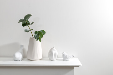 Ceramic figurines of birds on the fireplace. Corrugated vase with a branch of dried eucalyptus. Office decoration. Copy space. Scandinavian style