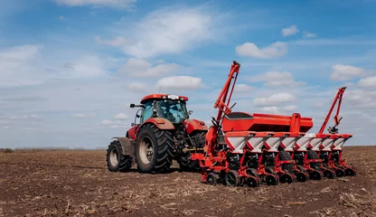 Foto op Aluminium Spring sowing season. Farmer with a tractor sows corn seeds on his field. Planting corn with trailed planter. Farming seeding. The concept of agriculture and agricultural machinery. © bondvit