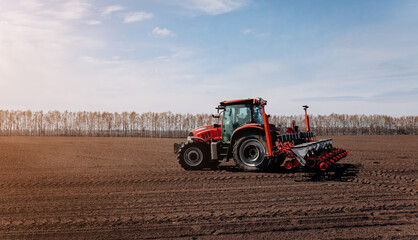 Spring sowing season. Farmer with a tractor sows corn seeds on his field. Planting corn with trailed planter. Farming seeding. The concept of agriculture and agricultural machinery.