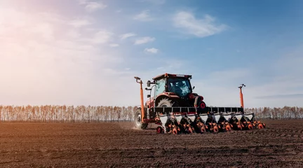 Foto op Plexiglas Spring sowing season. Farmer with a tractor sows corn seeds on his field. Planting corn with trailed planter. Farming seeding. The concept of agriculture and agricultural machinery. © bondvit
