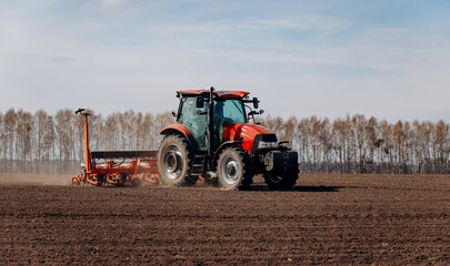 Fototapeta na wymiar Spring sowing season. Farmer with a tractor sows corn seeds on his field. Planting corn with trailed planter. Farming seeding. The concept of agriculture and agricultural machinery.