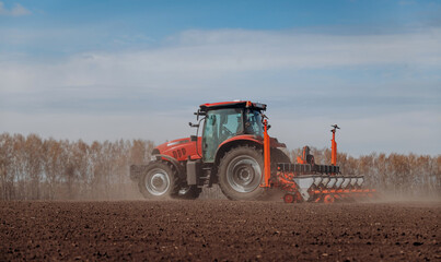 Obraz premium Spring sowing season. Farmer with a tractor sows corn seeds on his field. Planting corn with trailed planter. Farming seeding. The concept of agriculture and agricultural machinery.