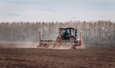 Spring sowing season. Farmer with a tractor sows corn seeds on his field. Planting corn with trailed planter. Farming seeding. The concept of agriculture and agricultural machinery.