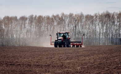 Spring sowing season. Farmer with a tractor sows corn seeds on his field. Planting corn with trailed planter. Farming seeding. The concept of agriculture and agricultural machinery.