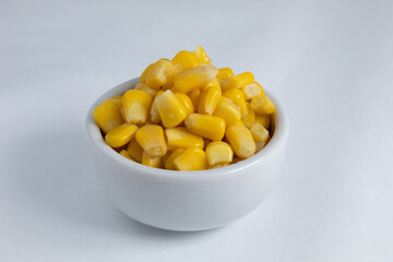 Small portion of sweet corn kernels, cooked and preserved, inside a small ceramic bowl. On white background