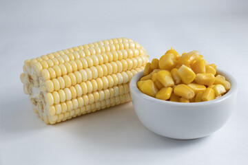 Corn on the cob split in half, raw and without straw, accompanied by cooked corn kernels, inside a ceramic bowl
