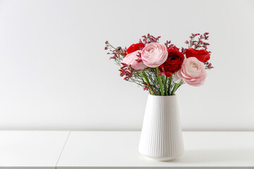 Fototapeta Bouquet of red and pink Persian buttercups on a white table. Scandinavian style. Place for text. Copy space obraz