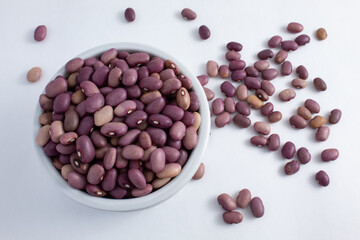 Brazilian purple beans seen from above in a white ceramic pot with a handful scattered around. Fresh, raw and healthy purple beans