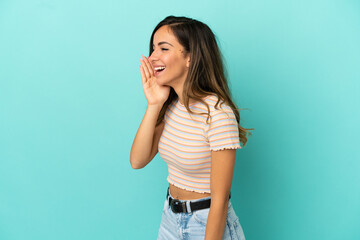 Young woman over isolated blue background shouting with mouth wide open to the side