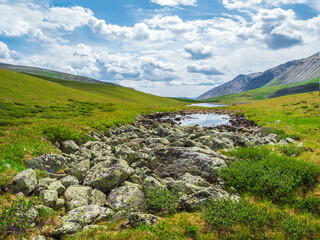 Fototapeta na wymiar Summer sunny highlands. Stone riverbed in the summer Alpine highlands. The riverbed without water, the drought at the summer. The riverbed is paved with stones.