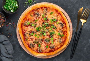 Fresh pizza with champignons, tomatoes, cheese and fresh herbs on a black background.