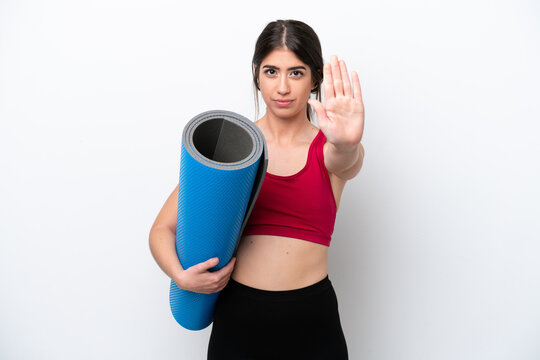 Young Sport Woman Going To Yoga Classes While Holding A Mat Isolated On White Background Making Stop Gesture