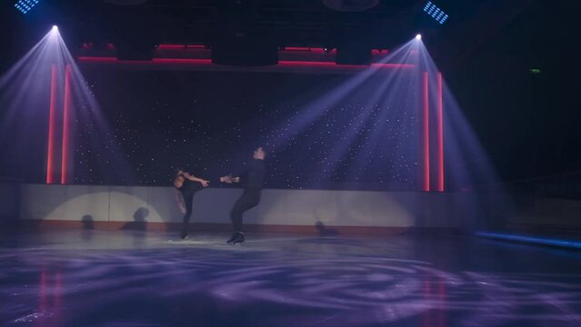 Technique of complex risky lift in pair figure skating. Woman slides backwards, man holds her leg, transfers to hovering over ice, olding both ankles with crossed arms.Dangerous element, slow motion.