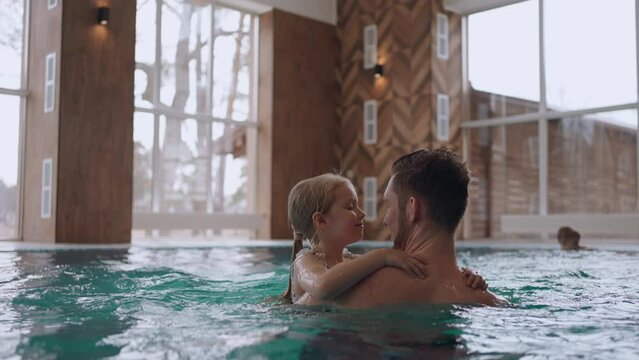 happy little girl is playing with her dad in swimming pool, recreation area and wellness center for family