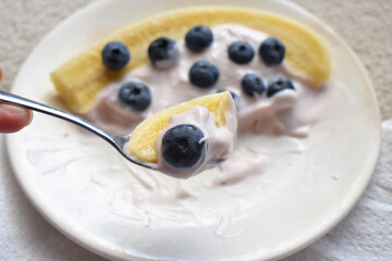 Close-up of a spoon with Fresh and tasty of organic blueberries, banana and yogurt a white plate. Healthy eating in morning.