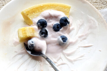 Close-up of a spoon with Fresh and tasty of organic blueberries, banana and yogurt a white plate. Healthy eating in morning.