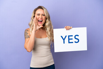 Young Brazilian woman isolated on purple background holding a placard with text YES and shouting