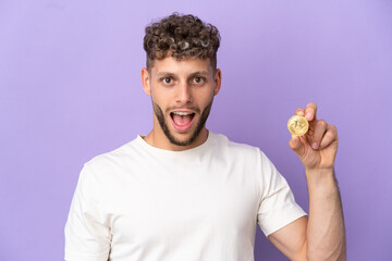 Young caucasian man holding a Bitcoin isolated on purple background with surprise facial expression