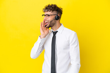 Telemarketer blonde man working with a headset isolated on yellow background shouting with mouth wide open to the lateral