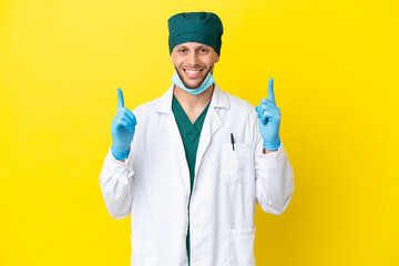 Surgeon blonde man in green uniform isolated on yellow background pointing up a great idea