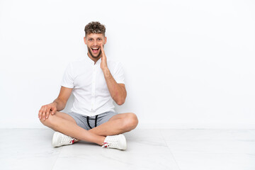Young blonde man sitting on the floor isolated on white background with surprise and shocked facial expression
