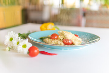 Scrambled eggs with bacon tomatoes and herbs on a white table
