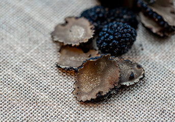 Truffles on a beige burlap. Sliced mushrooms. Black raw champignons on the surface. Top view. Dark blurred background. The artistic intend and the filters. Subject is out of focus.