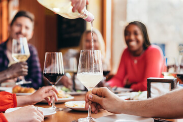 waiter pouring white wine into a glass with many diners