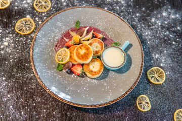 Cheesecakes with condensed milk and strawberries on a gray plate standing on a dark table