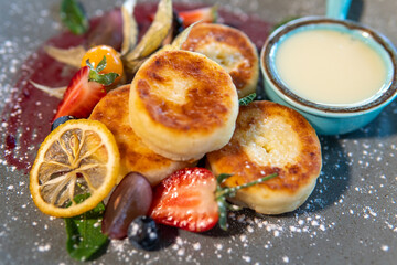 Cheesecakes with condensed milk and strawberries on a gray plate standing on a dark table