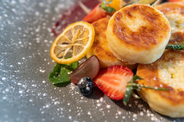 Cheesecakes with condensed milk and strawberries on a gray plate standing on a dark table