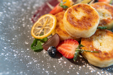Cheesecakes with condensed milk and strawberries on a gray plate standing on a dark table