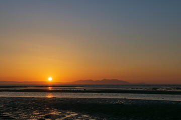 Sunset over the beach and mountain, horizon line yellow and orange shading reflection to water and sand. Focusing at surface shadow. Landscape nature scenery background.
