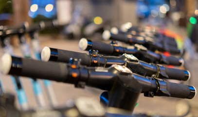 Obraz premium Electric kick modern scooters parked on city street at night. Eco alternative transport concept - Selective Focus.