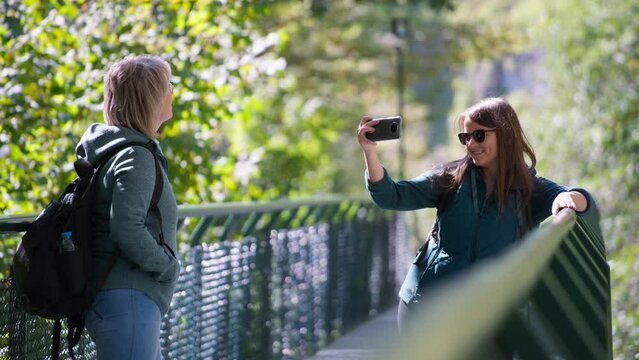 Mother and daughter standing on the bridge, while taking selfies with a phone. Slow motion. 