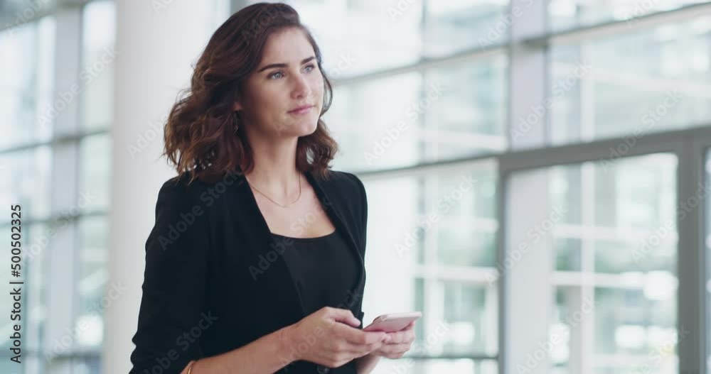 Wall mural Places to go, people to connect with. 4k video footage of a young businesswoman using a smartphone while walking through a modern office.