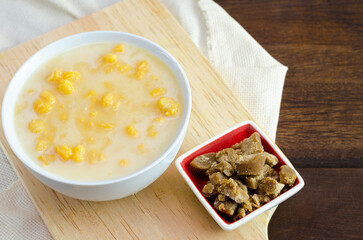 Traditional Colombian food called mazamorra,based on cooked corn dissolved in milk,accompanied with panela in pieces (sweet from sugar cane). Dark wooden background.