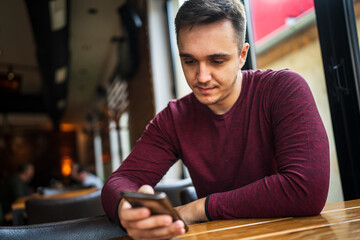 Young caucasian man sitting alone at cafe front view of one serious worried male while using mobile phone for texting or browsing internet or making a phone call copy space real people