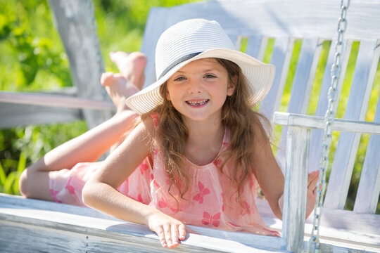 Child girl having fun on a swing. Adorable little girl having fun on a swing outdoor. Close up portrait of a beautiful girl in hat dreaming.