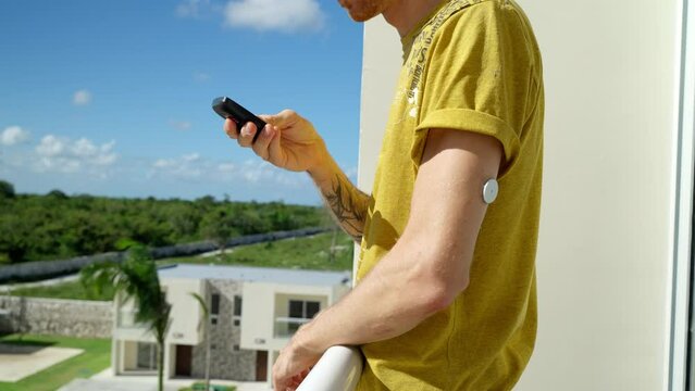 Young Adult Male Walking Towards Hotel Balcony And Checking Diabetes Levels On Left Arm With Freestyle Libre 2 Sensor. Side View