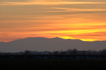 Beautiful evening panoramic landscape with bright setting sun over distant mountain peaks at sunset