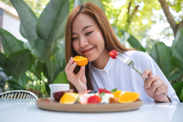 Portrait image of a young woman holding a piece of an orange while eating mixed fruits french toast brunch in restaurant