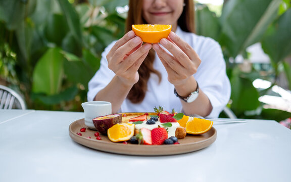 Closeup image of a young woman holding a piece of an orange while eating mixed fruits french toast brunch in restaurant