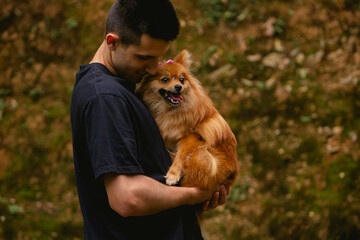 Brazilian man, in black t-shirt, holding a German spitz dog on his lap.