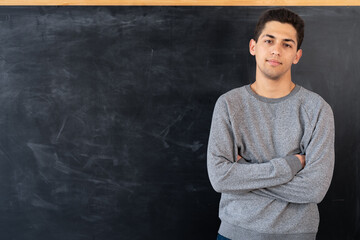 Happy young arab man standing with crossed arms on blackboard background, education concept,...