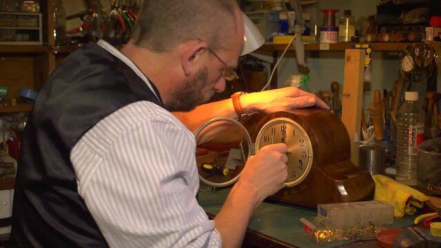Clockmaker fitting the hands on a clock, over shoulder.