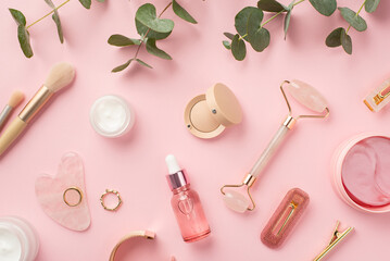 Fototapeta Top view photo of makeup brushes rose quartz roller gua sha pink eye patches glass bottles with serum cream eyeshadow lip gloss hairpins gold rings wristlet and eucalyptus on isolated pink background obraz