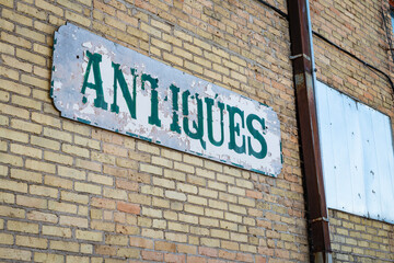 A well-weathered sign reading "antiques" is affixed to a brick wall to advertise a business.