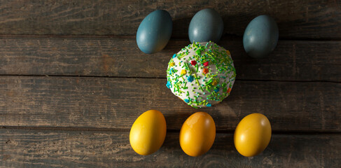 Painted eggs for Easter in the colors of the flag of Ukraine and an Easter cake in the center. Yellow and blue (cyan). On wood texture. Concept: food, holiday, war in Ukraine
