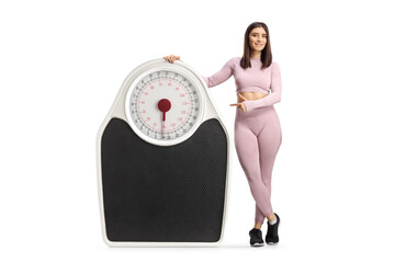 Full length portrait of a young fit woman in sportswear posing with a big scale and pointing